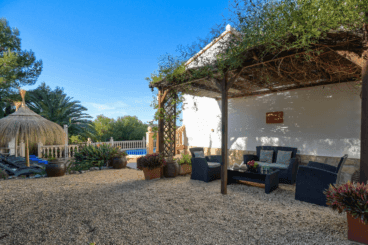 Jardín con gravilla y zona de comedor bajo una pérgola de madera