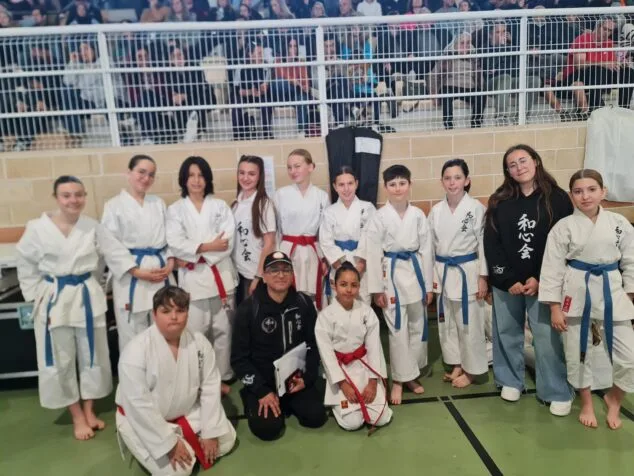 Grupo de jóvenes estudiantes de karate Washinkai y sus instructores posando en un gimnasio con público al fondo.