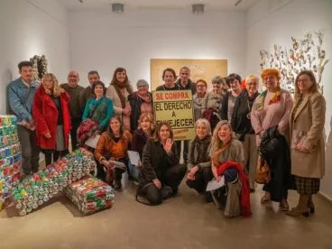 Grupo de personas posando en una galería de arte con una pancarta que dice 'Se compra el derecho a envejecer al contado'.