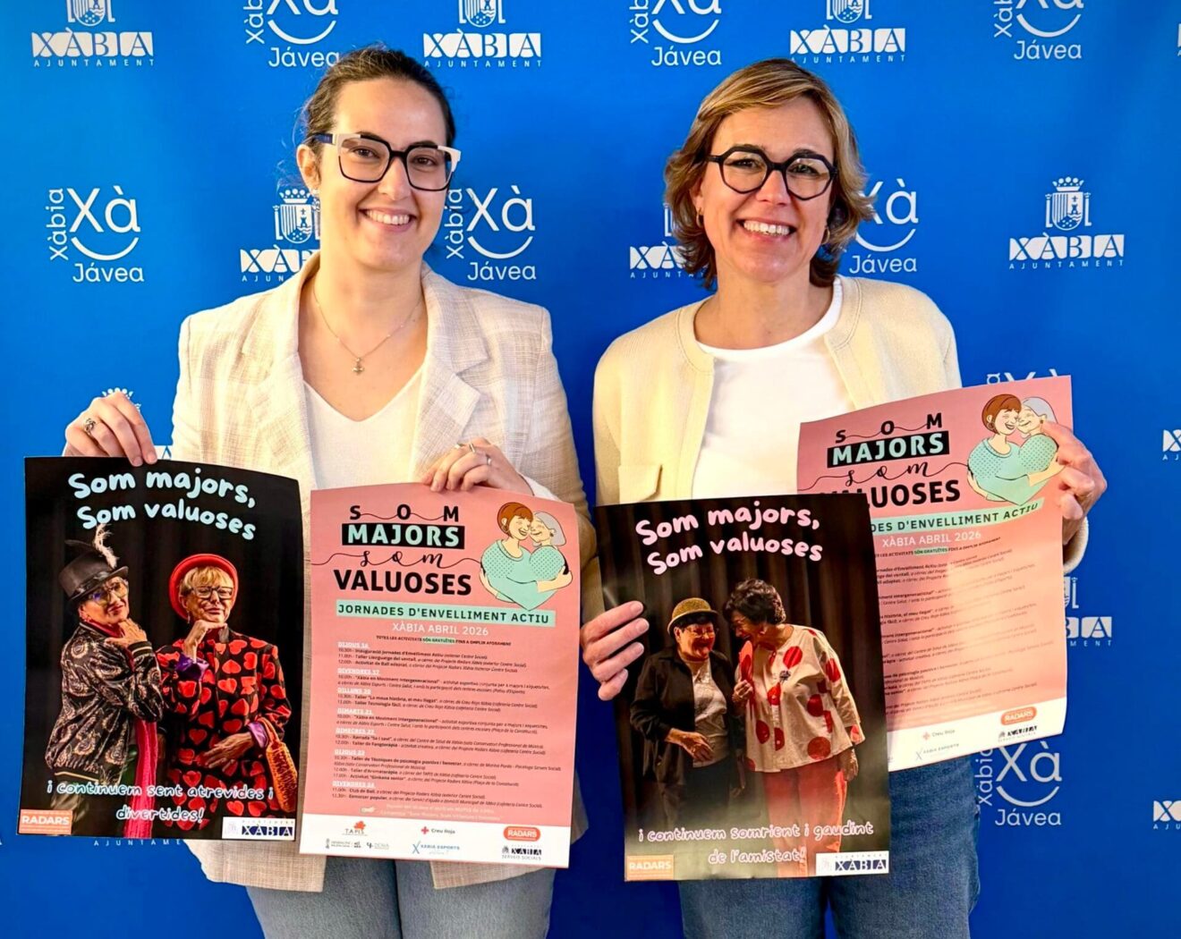 Rosa Cardona y Raquel Violero posan sosteniendo los carteles de las Jornadas de Envejecimiento Activo de Xàbia 2026.