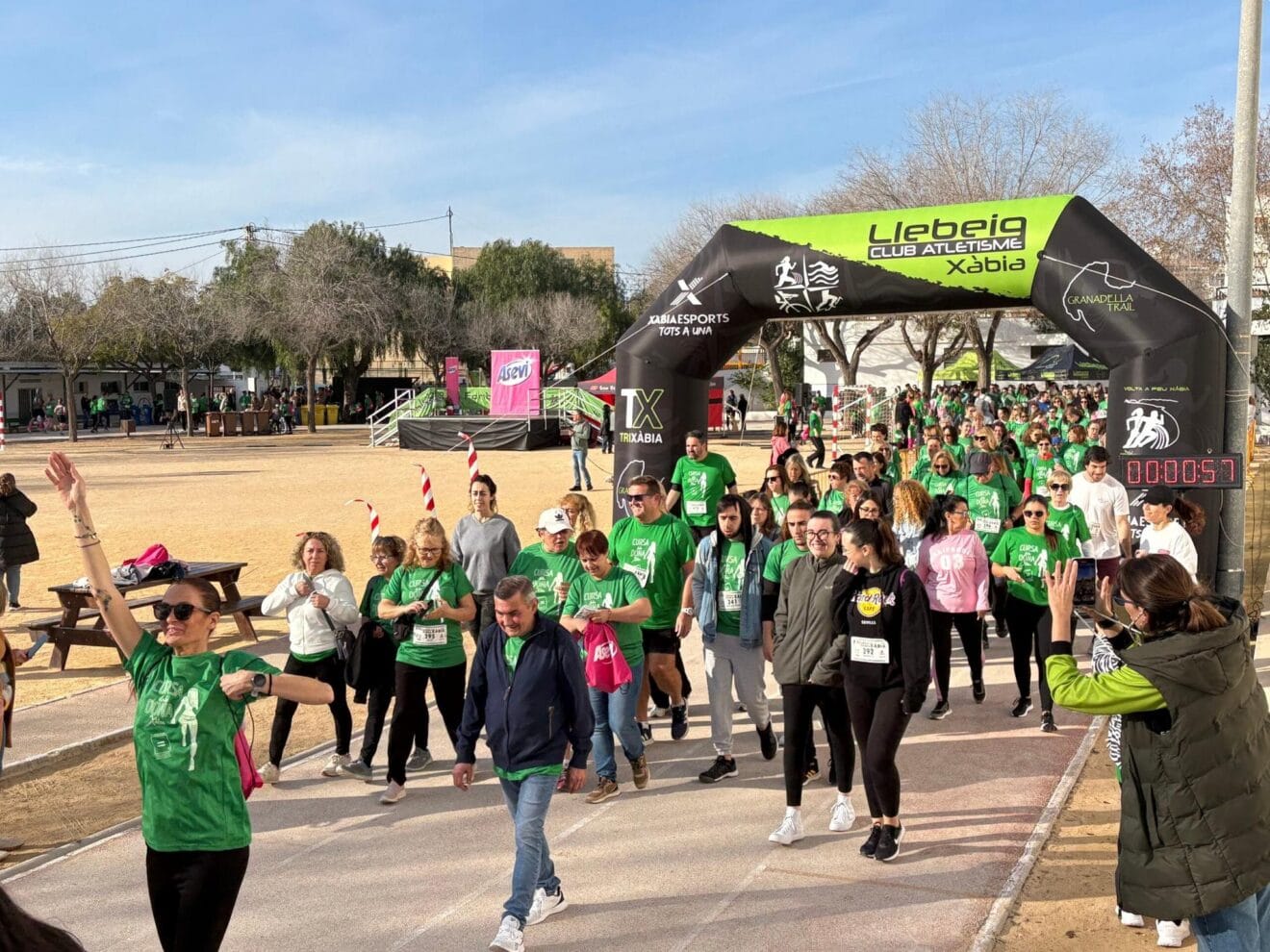 Multitud de participantes caminando y corriendo en la salida de la Cursa de la Dona de Xàbia bajo un arco del Club Atletisme Llebeig.