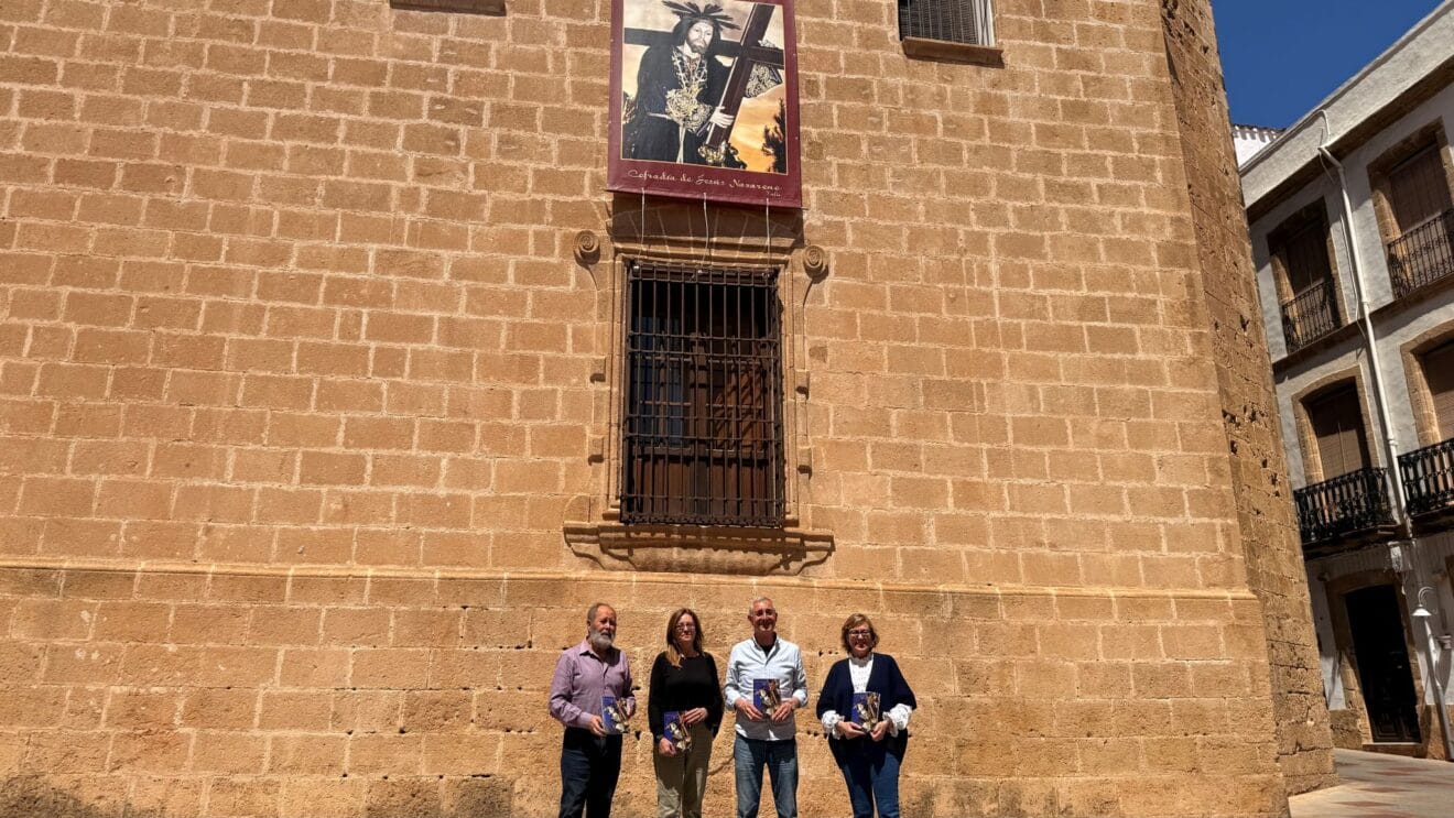 El equipo organizador exhibe los folletos de las fiestas del Nazareno ante la fachada de la iglesia
