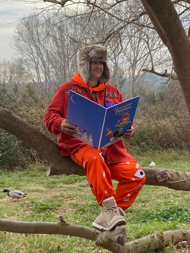 Imagen: Paco Cholbi sentado en una rama sosteniendo el libro "El monstre Petorro".