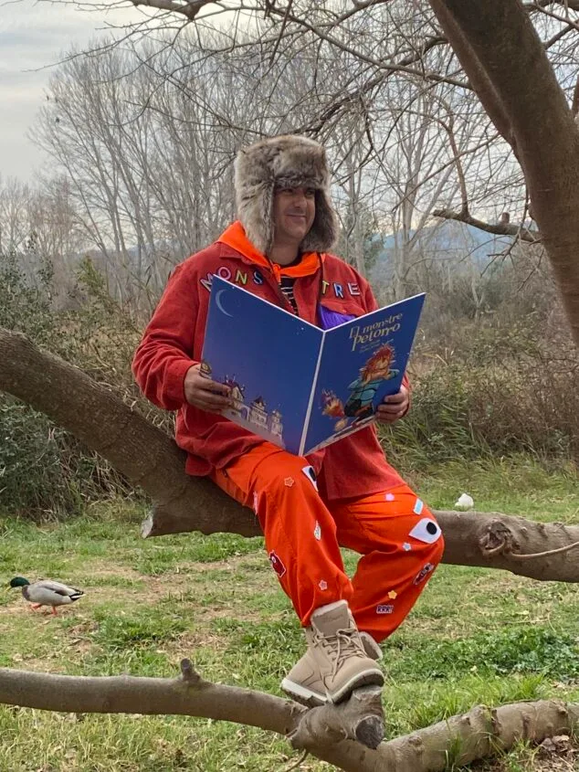 Imagen: Paco Cholbi sentado en una rama sosteniendo el libro "El monstre Petorro".