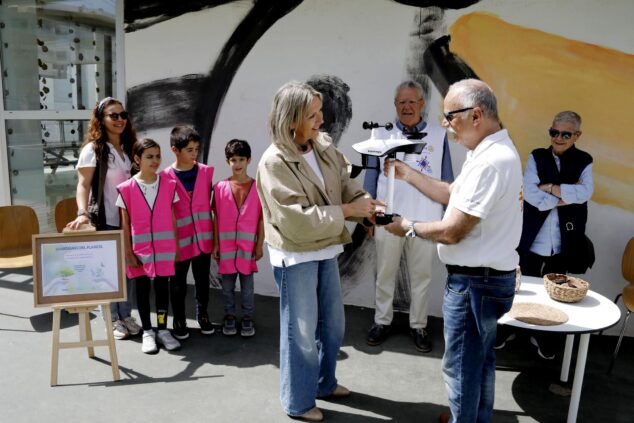 Imagen: Un miembro del Rotary Club entrega una estación meteorológica a la directora de un colegio ante la mirada de varios estudiantes con chalecos reflectantes.