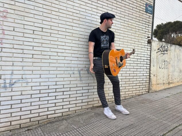 Imagen: Tafol posando con una guitarra acústica contra una pared de ladrillo