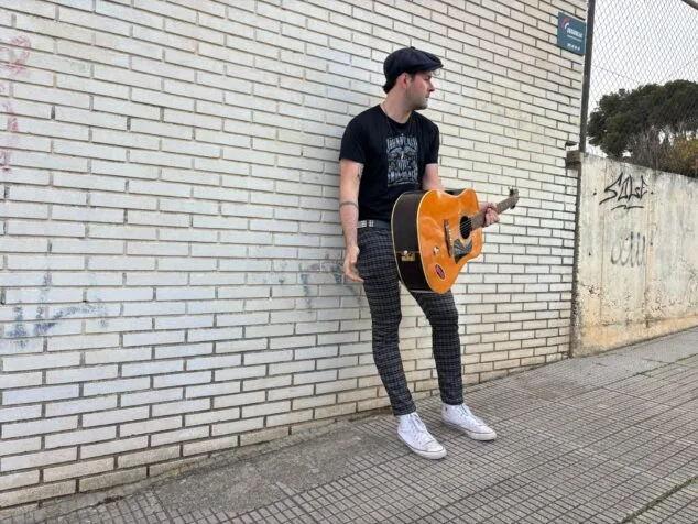Tafol posando con una guitarra acústica contra una pared de ladrillo