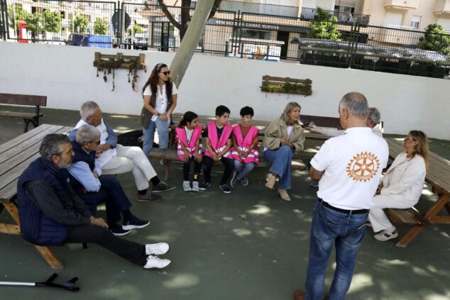 Imagen: Miembros del Rotary Club Jávea, uno de ellos con camiseta del logo, conversan con alumnos con chalecos reflectantes y docentes en el patio del Colegio Port de Xàbia.