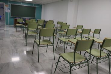 Aula vacía con filas de sillas y pupitres verdes orientados hacia una pizarra.