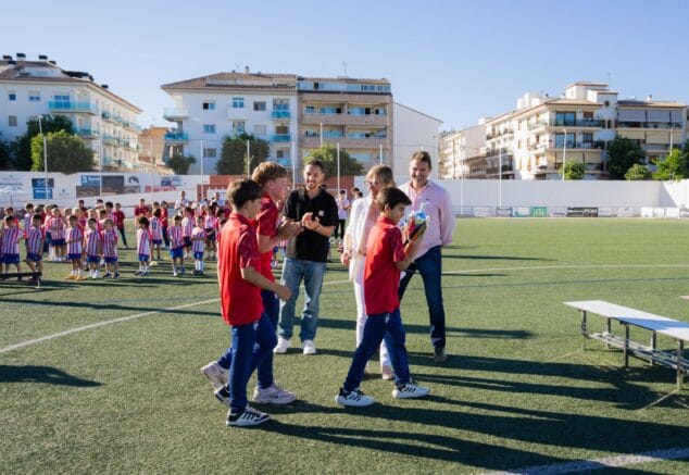 Imagen: Jugadores jóvenes del CD Jávea reciben un trofeo en el campo de fútbol durante la fiesta de final de temporada, con adultos aplaudiendo.