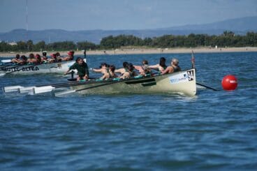 Dos embarcaciones de remo con tripulaciones femeninas disputando una carrera en el mar cerca de la costa.