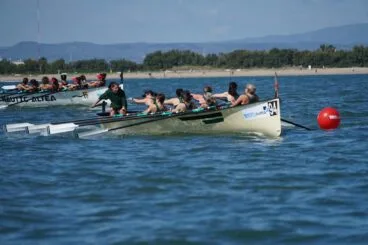 Dos embarcaciones de remo con tripulaciones femeninas disputando una carrera en el mar cerca de la costa.