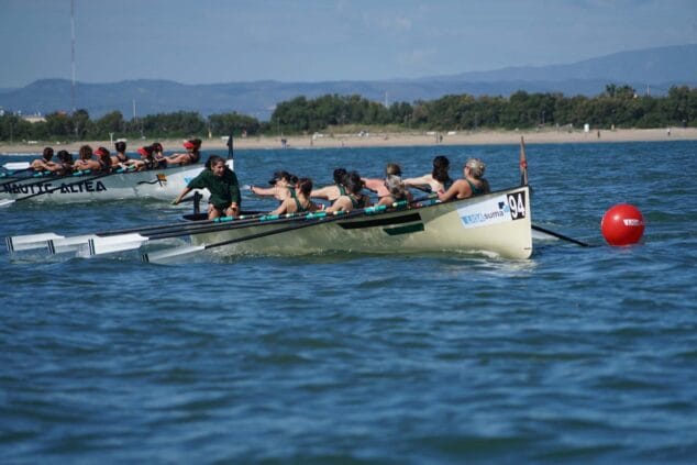 Dos embarcaciones de remo con tripulaciones femeninas disputando una carrera en el mar cerca de la costa.
