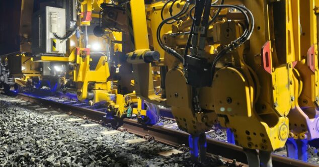 Primer plano de maquinaria ferroviaria amarilla realizando trabajos de bateo en las vías del TRAM d'Alacant durante la noche.