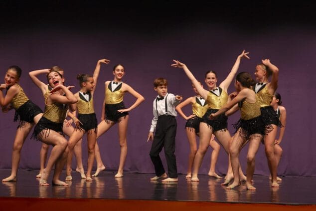 Imagen: Grupo de jóvenes bailarines de Endanza en el escenario con trajes negros y dorados durante una actuación.
