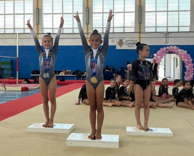 Tres jóvenes gimnastas en un podio recibiendo medallas en un pabellón deportivo en Castellón.