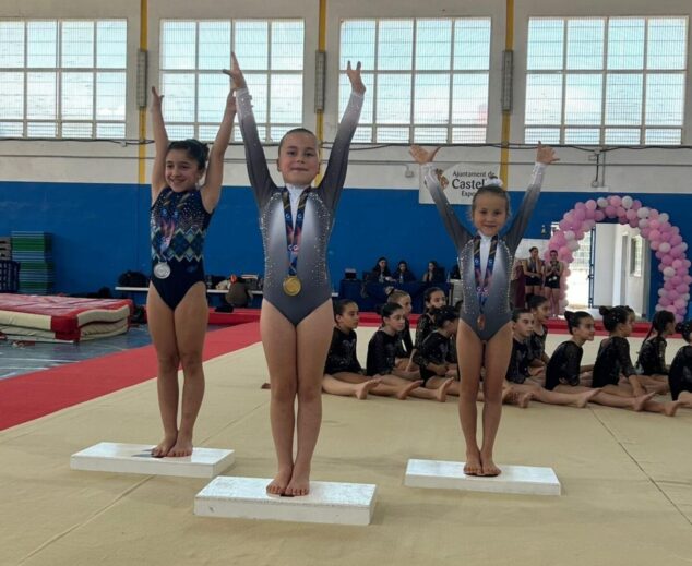Tres jóvenes gimnastas con medallas posan en un podio deportivo.