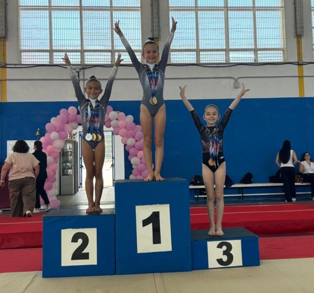 Tres jóvenes gimnastas con medallas posando en un podio.