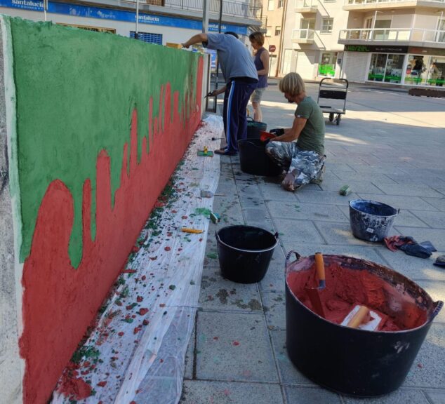 Personas pintando un mural rojo y verde en una plaza pública de Xàbia.