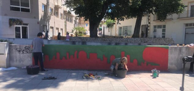 Imagen: Varias personas pintando un mural con siluetas rojas sobre fondo verde en la Plaça de la Constitució de Xàbia.