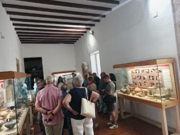 Grupo de visitantes observando vitrinas con piezas arqueológicas durante una visita guiada en el interior del Museu Soler Blasco.