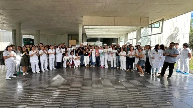 Grupo numeroso de trabajadores sanitarios con batas blancas y uniformes protestando con pancartas en la entrada techada del Hospital de Dénia.