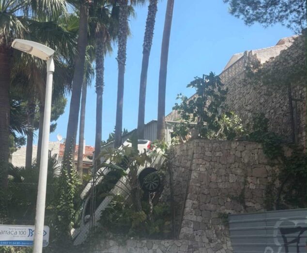 Imagen: Coche blanco accidentado colgando de un muro de piedra en Javea.