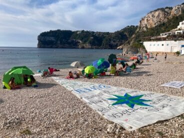 La Cala de la Barraca con turistas y la vela con mensaje reivindicativo por la educación pública