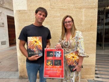 Rubén Atienza y Mavi Pérez sostienen el cartel rojo del Certamen Circ i Foc y el libro de Fogueres Xàbia 2026 frente a un edificio de piedra.