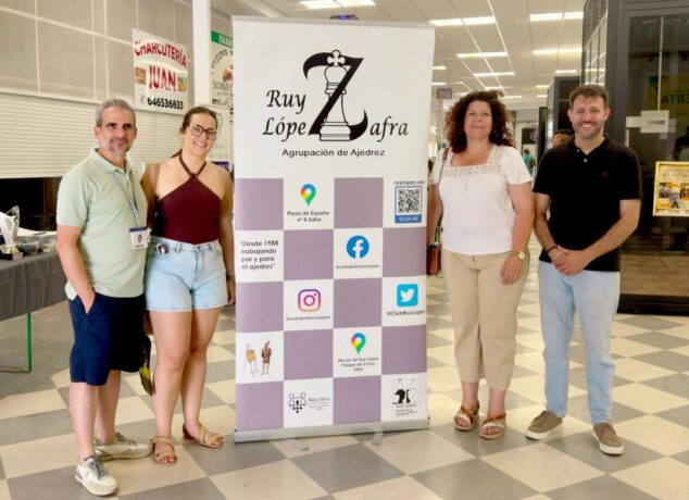 Imagen: Cuatro personas posan de pie delante de un banner promocional de la Agrupación de Ajedrez Ruy López de Zafra.