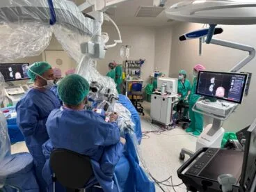 Equipo médico en quirófano realizando una neurocirugía con microscopio y monitores de visualización.
