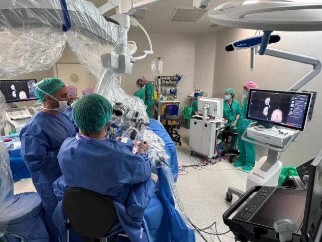 Equipo médico en quirófano realizando una neurocirugía con microscopio y monitores de visualización.