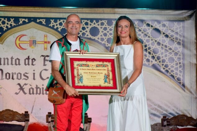 Imatge: Mavi Pérez lliura un quadre de reconeixement a César Rodríguez, Pregoner de les festes, en un escenari.