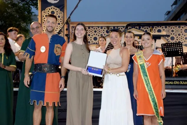 Entrega de una placa de reconocimiento en un escenario con representantes de las fiestas de Moros y Cristianos de Xàbia.