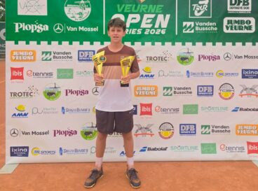 El tenista Luca Barclay sostiene sus dos trofeos de campeón del torneo Open Veurne frente al panel de patrocinadores.