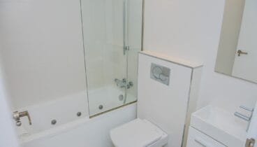 Moderno cuarto de baño blanco con bañera de hidromasaje, mampara de cristal, inodoro suspendido y lavabo rectangular. Azulejos blancos y grifería cromada