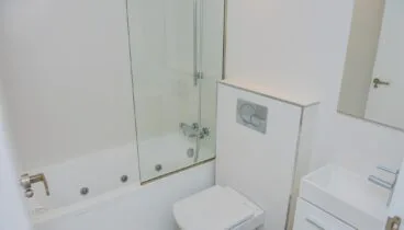 Moderno cuarto de baño blanco con bañera de hidromasaje, mampara de cristal, inodoro suspendido y lavabo rectangular. Azulejos blancos y grifería cromada