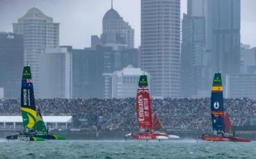 Catamaranes F50 de España, Gran Bretaña y Australia compitiendo en una regata de SailGP bajo la lluvia y con edificios de fondo.