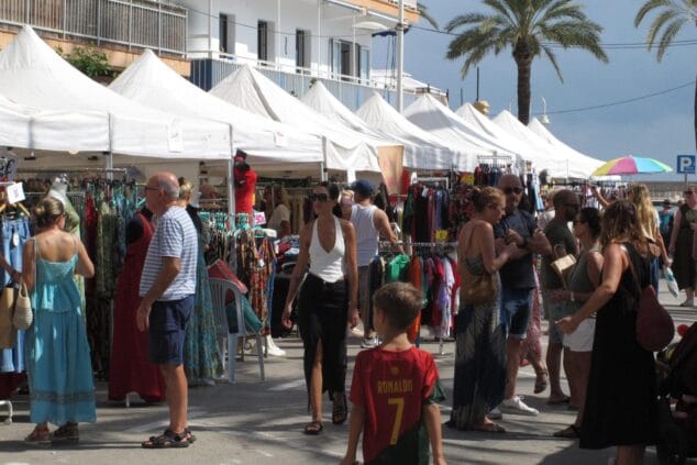 Fotografía de varias personas mirando ropa en los puestos de un mercado al aire libre con carpas blancas bajo un día soleado en Xàbia.