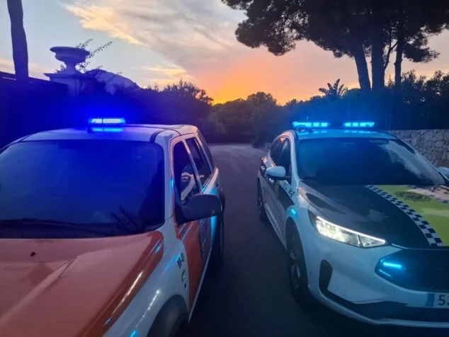 Imagen: Dos vehículos de policía y emergencias con luces azules parpadeando al atardecer en Xàbia.