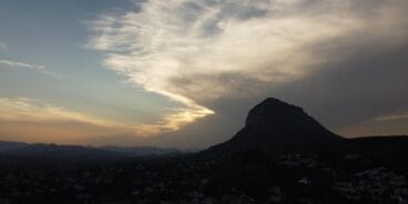 Paisaje con la silueta de la montaña del Montgó al fondo, bajo un cielo dramático con nubes y luz crepuscular sobre la población de Xàbia.