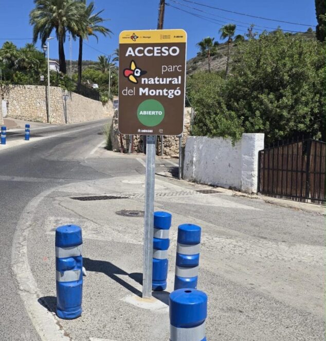 Imagen: Señal marrón de 'ACCESO parc natural del Montgó' con un círculo verde debajo que dice 'ABIERTO', ubicada junto a una carretera.