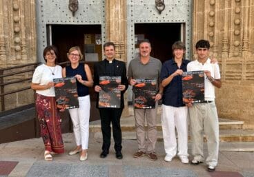 La alcaldesa de Xàbia, el párroco y varios organizadores posan con el cartel de la Nit de Sant Bartolomé frente a la iglesia.