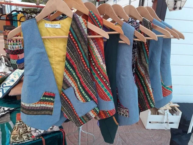 Varios chalecos hechos a mano con telas vaqueras y estampadas colgando en un puesto de mercado.