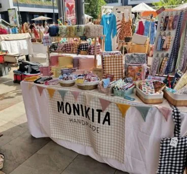 Puesto de venta de productos textiles artesanales de Monikita Handmade en un mercado al aire libre.