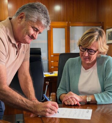 Rosa Cardona observa a un hombre firmando un documento de AMJASA en una oficina.