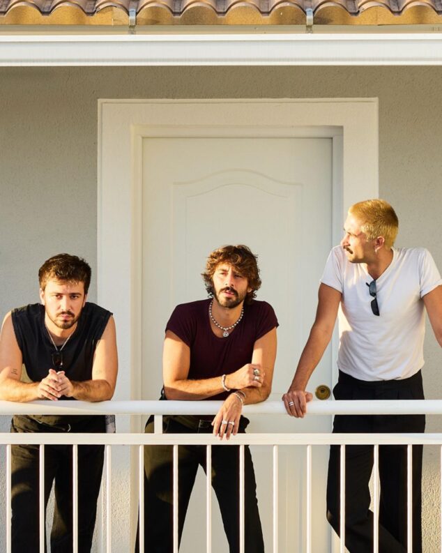 Imagen: Retrato de los tres miembros de la banda de música Éxtasis apoyados en una barandilla blanca.