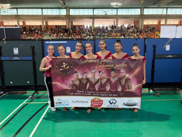 Imagen: El equipo de gimnasia rítmica Cadete Base del CD Montgó Xàbia con su entrenadora sosteniendo una pancarta en un pabellón.