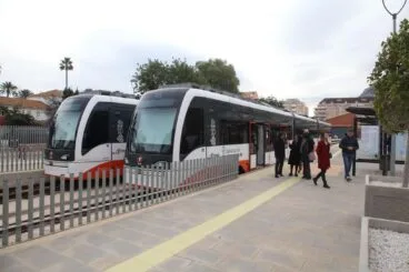 Pasajeros esperando en un andén del TRAM d'Alacant junto a dos trenes.